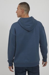 Marineblaue Kapuzenjacke aus weichem Material, mit einer großen Kapuze, gerippten Bündchen und Saum, lockerem Schnitt und minimalistischem Design.