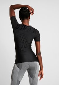 Svart kortärmad atletisk topp med en åtsittande design och ribbad textur, ihop med mönstrade leggings med vertikala ränder.