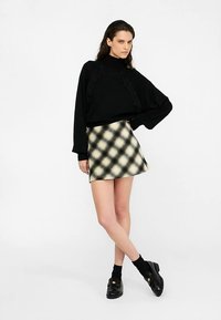 Pull noir oversize avec des accents texturés, assorti à une mini-jupe à motifs dans des tons beige et noir, porté avec des chaussures et des chaussettes noires.