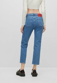 Blå denimjeans med rak passform, med två bakfickor och en röd etikett vid midjan, i kombination med svarta plattformsskor.