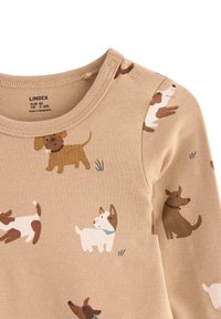 Beige langærmet top med en blød tekstur, der prydes af forskellige hundeillustrationer i brune og hvide nuancer, rund halsudskæring og trykknaplukninger ved skulderen.