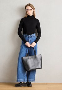 Svart läder tote-väska med två handtag. Modellen bär en figurnära svart polotröja och högmidjade blå vida jeans, kompletterat med svarta skor.