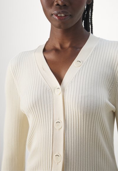 Off-white ribbestrikket cardigan med V-hals, har fem runde knapper, og varierer i tekstur langs kroppen og ermene.