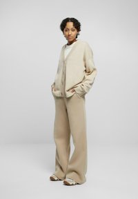 Beige cardigan with oversized fit, v-neck, and buttons; paired with wide-leg, matching beige pants; smooth texture, casual design.