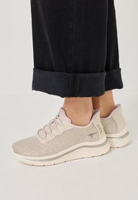 Pantofi sport bej deschis cu superior din plasă, închidere cu șireturi și o talpă groasă din cauciuc alb. Prezintă un logo mic și accente șterse.