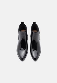 Paire de bottines noires brillantes à bouts pointus avec panneaux latéraux élastiques et languettes de tirage, vues de dessus sur fond blanc.