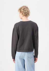 Black sweatshirt with a relaxed fit, ribbed neckline, dropped shoulders, and a cropped hem. Worn with light blue jeans.