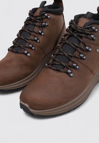 Botas de senderismo de cuero marrón con acabado liso, cuello de malla negro y cordones duraderos con detalles en negro y naranja para un mejor agarre.