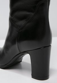 Bottine en cuir noir avec une texture lisse, un design classique et courbé, et un talon épais à finition brillante.