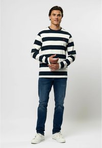 Marineblauw en witte gestreepte longsleeve shirt met geribde manchetten, gecombineerd met donkere jeans en witte sneakers. Klein rood logo op de borst.