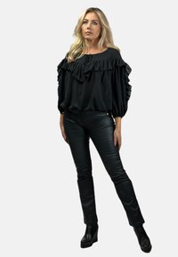 Czarna bluzka bez ramiączek z falbanami, zestawiona z czarnymi skórzanymi spodniami i botkami na obcasie. Gładka tekstura, dopasowany krój.