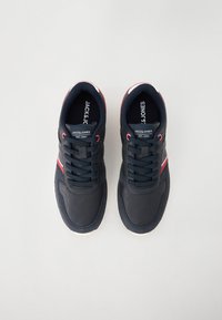 Marineblå sneakers med et teksturert læroverdel, kontrasterende røde og hvite detaljer, og tykke sorte lisser, med en polstret såle.