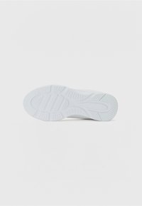 Semelle de sneaker blanche avec des motifs de grip texturés et des designs angulaires, présentant une finition lisse et un talon légèrement surélevé.