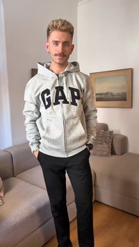 Szara bluza zip-up z napisem "GAP" w czarnych literach, w zestawie z czarnymi spodniami. Prosty design, brak widocznych wzorów lub akcentów. Luźny krój.