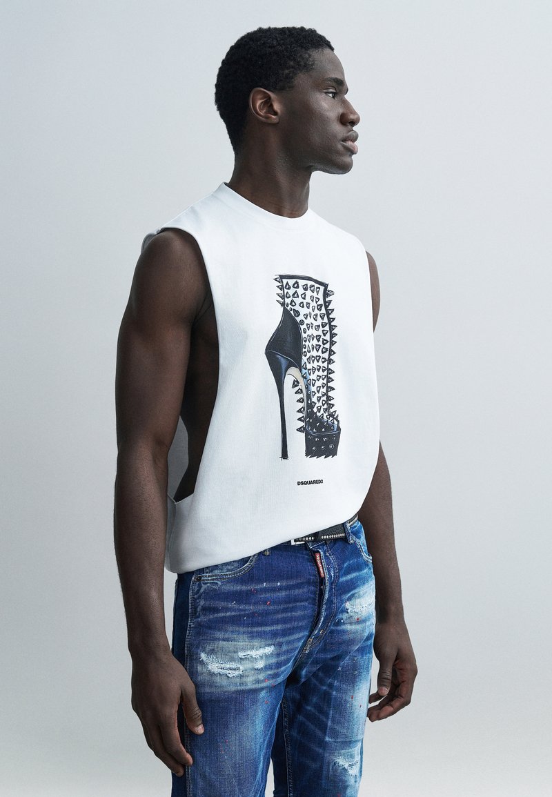 Λευκό αμάνικο πουκάμισο με γραφικό ενός ψηλοτάκουνου παπουτσιού διακοσμημένου με αγκίδες, συνδυασμένο με μπλε τζιν με φθορές.