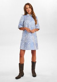 Blauwe jurk met bloemenprint, voorzien van een kraag en korte pofmouwen. Gecombineerd met bruine kniehoge laarzen. Gemaakt van een katoenmix.
