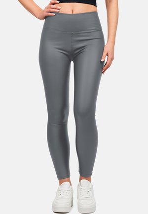 Leggings grigi alti in vita realizzati in un materiale liscio e elastico, con un design aderente e abbinati a sneakers bianche.