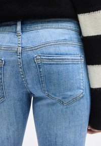 Ανοιχτό μπλε τζιν παντελόνι με στενή εφαρμογή, με δύο πίσω τσέπες και διακριτικές ραφές. Το υφασμάτινο υλικό με υφή φαίνεται στην εικόνα.