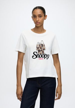 Frau trägt ein weißes T-Shirt mit einem Tarnmuster Snoopy-Hundehütte und schwarzem Snoopy-Text, kombiniert mit dunkelblauen Jeans.