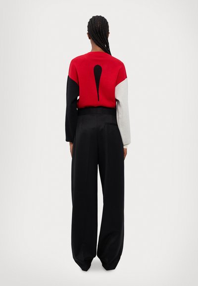 Maglione lavorato a maglia rosso, nero e bianco con un design a goccia sul retro; abbinato a pantaloni neri a vita alta e a gamba larga.