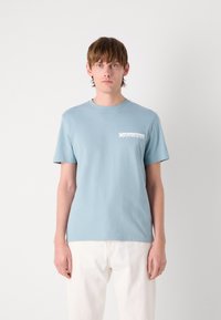 Šviesiai mėlynas medvilninis marškinėliai su apvaliu kaklu ir trumpomis rankovėmis. Kairėje krūtinės pusėje yra kišenė su balta Calvin Klein logo. Paprastas dizainas.