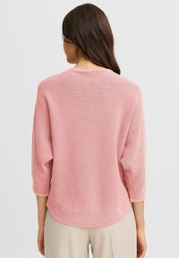Maglione rosa lavorato a maglia con texture a coste, scollatura rotonda e maniche 3/4. Vestibilità casual con orlo leggermente curvo.