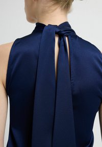 Granatowy, bezrękawnik wykonany z gładkiej tkaniny, z tylnym wiązaniem i wycięciem typu keyhole przy szyi dla dodatkowego efektu.