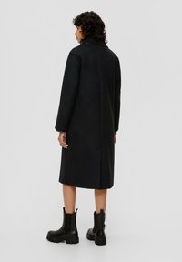 Schwarzer Wollmischungs-Mantel mit geradem Schnitt, langen Ärmeln und nichtched Kragen. Kombiniert mit schwarzen Leder-Stiefeletten.