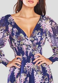 Marineblauwe bloemenjurk met een diepe V-hals, een geplooide gerimpelde bovenkant, lange doorzichtige mouwen en roze- en groene bloemenprints overal.