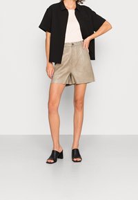 Maglietta nera a maniche corte, pantaloni corti beige con una texture a motivo coccodrillo, e mule nere aperte con tacco a blocco.
