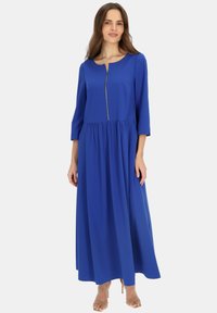 Niebieska maxi sukienka z rękawami o długości trzech czwartych, zapinana na zamek z przodu, z marszczoną talią i gładką teksturą. Ma rozszerzany krój.