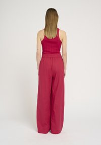 Ribbed, hihaton toppi tummanpunaisena yhdistettynä leveylahkeisiin, korkeavyötäröisiin housuihin, jotka ovat sävyltään samansuuntaiset ja joissa on elastinen vyötärö.