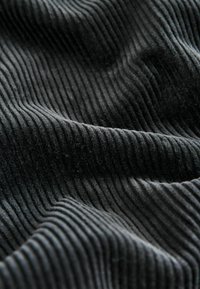 Black ribbed fabric with a soft texture, featuring parallel ridges. The material appears thick and plush, creating a wavy pattern.