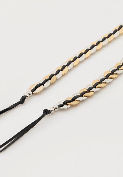Δύο πλεκτά λουριά με εναλλασσόμενους χρυσούς και ασημένιους οβάλ μεταλλικούς κρίκους συνδεδεμένους με μαύρα κορδόνια σε λευκό φόντο.