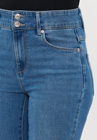 Jeans de mezclilla azul de talle alto con una textura suave, cierre de dos botones y costuras en contraste, que cuentan con bolsillos delanteros y un diseño ajustado.