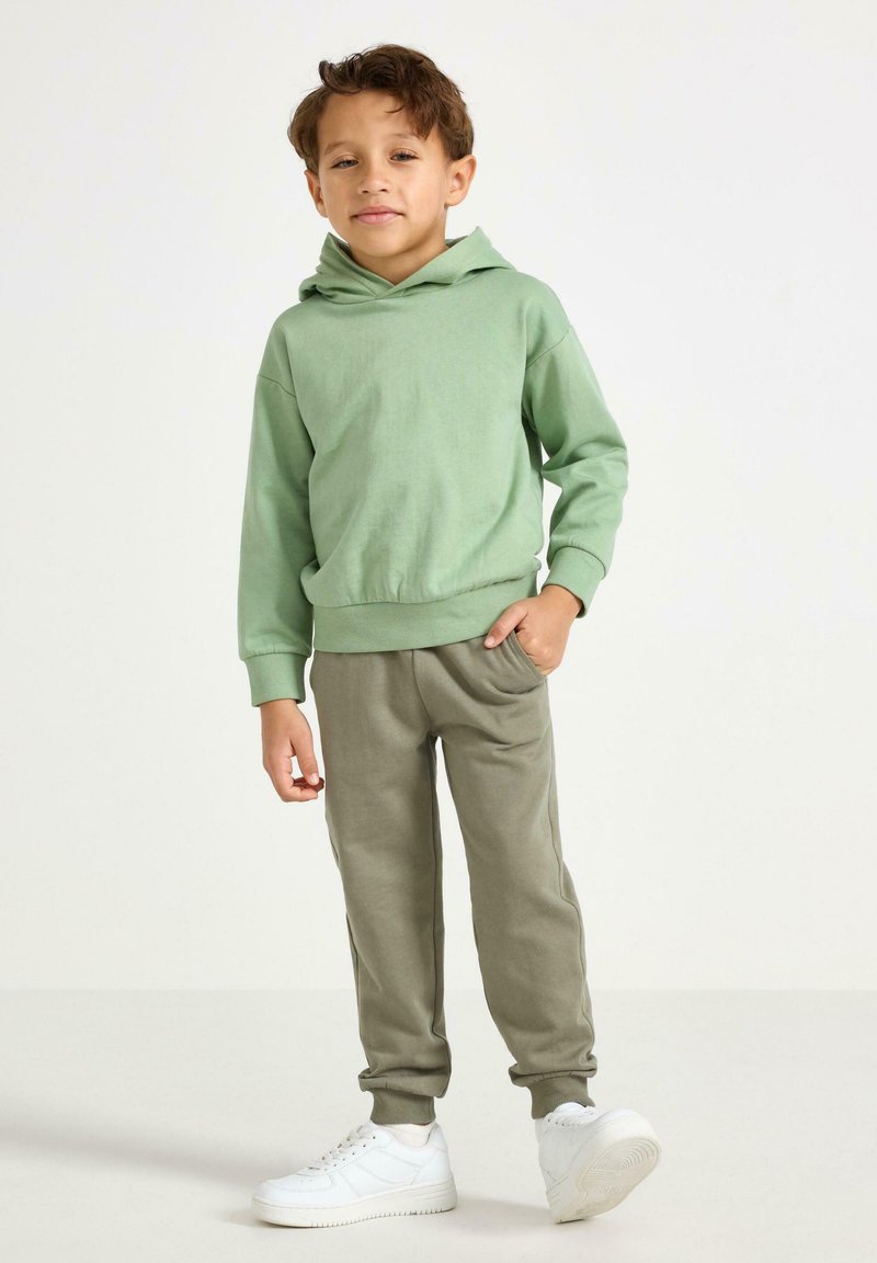 Grøn bomulds-hoodie og olivengrønne joggers, begge med afslappet pasform, kombineret med hvide sneakers, der viser et simpelt og behageligt design.