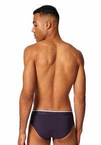 Slip blu scuro con un elastico bianco in vita, superficie liscia e design aderente, visto da dietro.