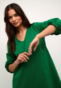 Grön oversized klänning, huvudsakligt av bomullsmaterial, V-ringning, sammanknippade trekvartsärmar, slät textur, inga synliga mönster eller beslag.