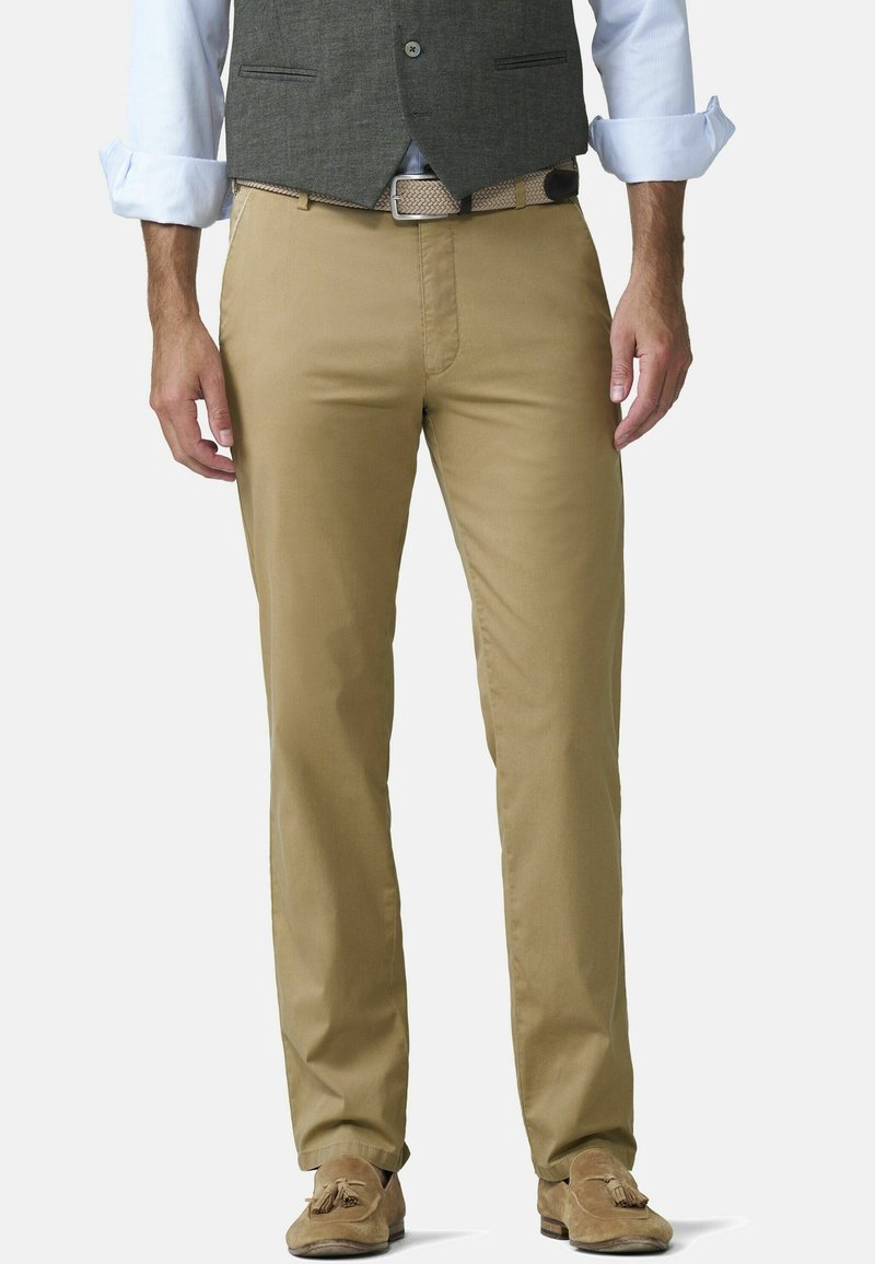 Homme portant un pantalon chino beige avec une ceinture tissée, une chemise bleu clair retroussée, un gilet gris et des mocassins en daim marron à glands.