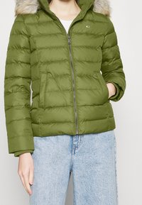 Grøn pufferjakke med lynlås, quiltet design og hætte med pelskant. Har sidelommer og ribbede manchetter. Letvægts, vandafvisende stof.