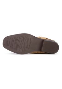 Botín de ante en color topo con una suela de goma marrón texturizada. Presenta un tacón plano y un diseño minimalista sin elementos de hardware visibles.