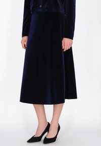 Marineblauwe fluwelen A-lijn rok met een gladde textuur, met een uitlopende silhouet, gecombineerd met klassieke zwarte puntige hakken.
