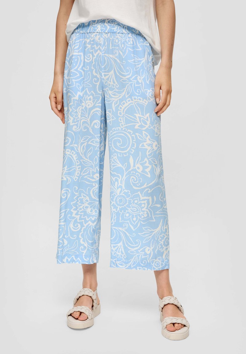 Lichtblauwe wijde broek met witte bloemenpatronen en een elastische tailleband, gecombineerd met crèmekleurige gevlochten sandalen.