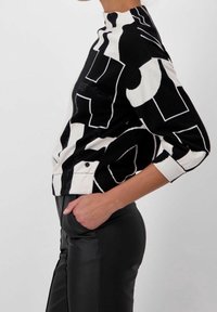 Maglione a tinta unita bianco e nero con collo alto, maniche a tre quarti e dettagli texturizzati. Abbinato a pantaloni in pelle nera.