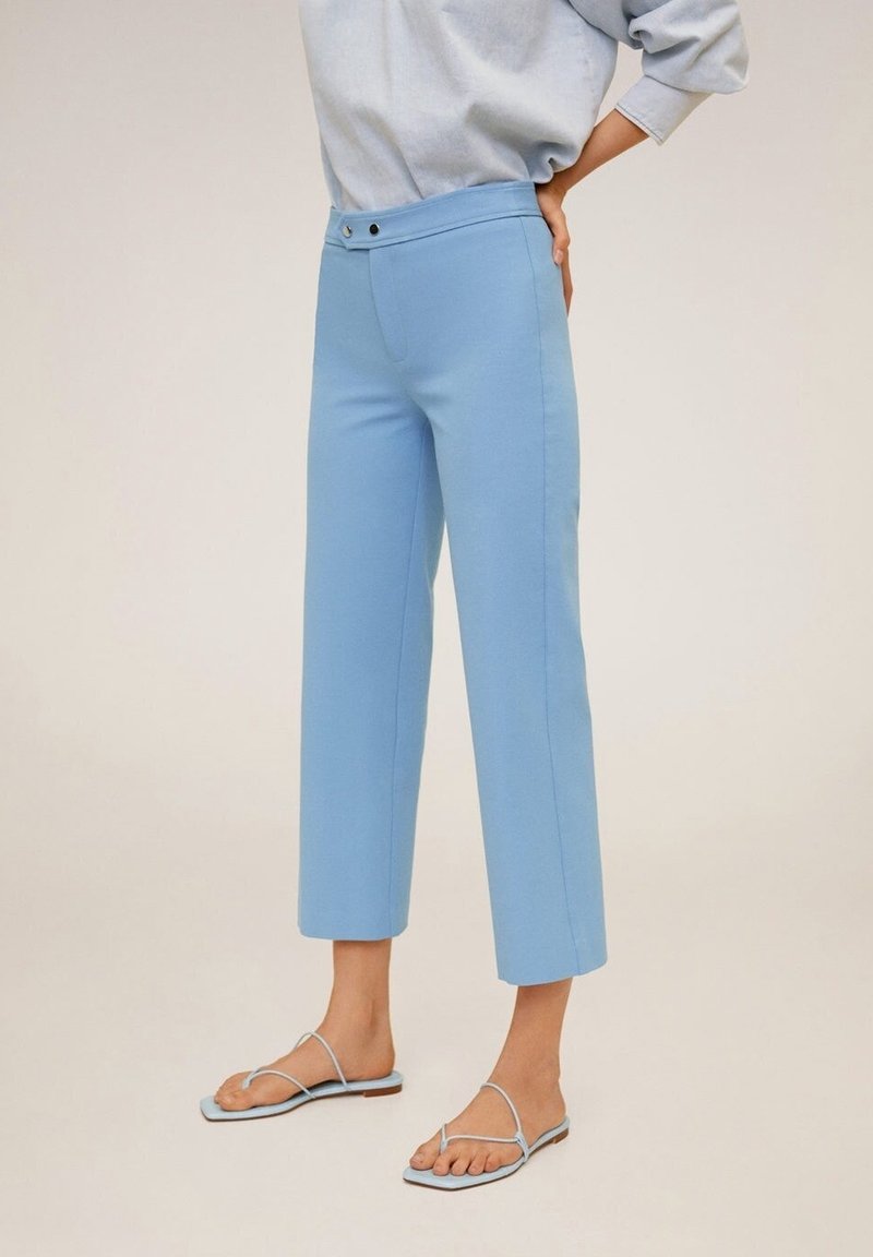Pantalons courts bleu clair en tissu lisse, avec une taille haute, deux boutons à l'avant et un design à jambes droites. Associés à des sandales bleues.