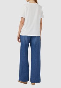 T-shirt en coton blanc à manches courtes associé à un pantalon en denim bleu taille haute, à jambes larges, et des chaussures beiges.