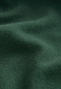 Tissu tricoté vert foncé avec des coutures visibles et de légers plis créant de douces ombres et une texture.