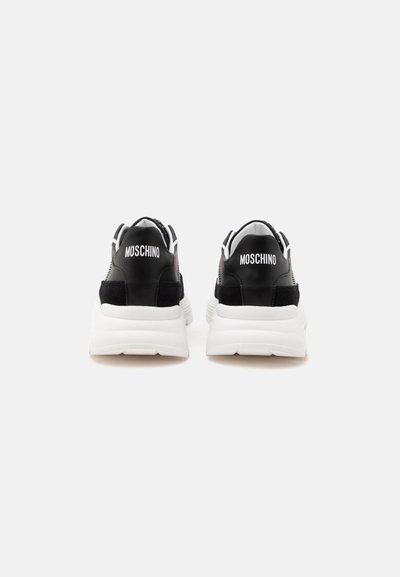 Paire de baskets Moschino noires et blanches vues de dos avec des semelles blanches épaisses et le nom de la marque en lettres blanches sur les talons.