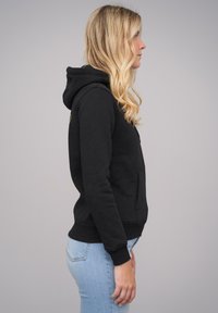 Black hoodie made from soft fabric, featuring a front pocket, ribbed cuffs, and a drawstring hood. Shown from the side with light jeans.