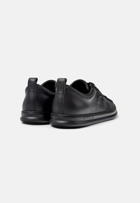 Sneaker in pelle nera con texture liscia, forma arrotondata e tallone imbottito. Presenta un branding discreto sul lato e cuciture minime.
